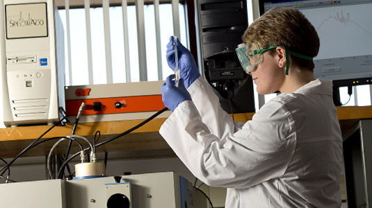 Student in lab coat examines samples in laboratory.